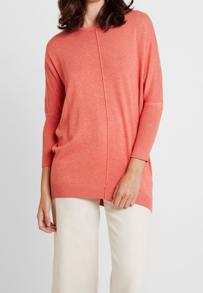 Koronkowy, oversize sweter w kolorze koralowym, z luźnym krojem, ryflowanymi mankietami oraz detalem wzdłuż środkowego szwu. Miękka faktura, idealna na codzienne wyjścia.