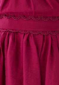 Fuchsia-farbenes Stoffkleidungsstück mit einer strukturierten, gewellten Borte und Falten. Weiche, glatte Textur mit einer reichen, lebendigen Farbe.