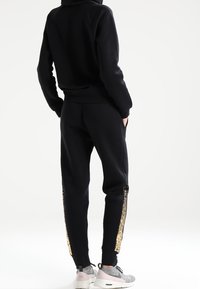 Svart hoodie och matchande joggers med guldpaljetter på sidorna. Sneakers har en ljusrosa och grå färgschema.