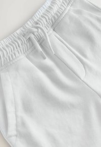 Pantalons de survêtement blancs avec une finition texturée, dotés d'une taille élastique avec cordon de serrage et de poches latérales. Tissu lisse et design décontracté.