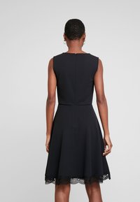 Czarna sukienka bez rękawów z dopasowanym gorsetem, rozkloszowanym dołem i falbaniastym koronkowym wykończeniem u dołu. Gładki materiał o subtelnej fakturze.