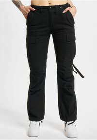 Black cargo pants with a relaxed fit, featuring multiple pockets, drawstring cuffs, and a smooth texture. Worn with white sneakers.