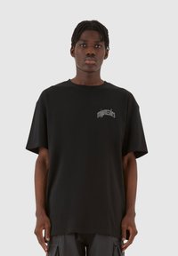 Fekete pamut, oversized póló, bal mellen egy kis szürke logóval. A póló kerek nyakú és rövid ujjú.