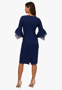 Navyblaues Kleid mit transparenten Rüschenärmeln, figurbetontem Schnitt, knielang, Schlitz hinten und verdecktem Reißverschlussdetail am Hals.