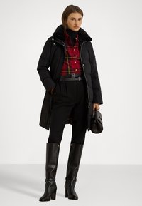 Melna polsterēta jaka ar mākslīgās kažokādas apkakli, apvienota ar sarkanu rūtainu krekli, augsto jostasvietu melnām biksēm un melniem ādas zābakiem līdz ceļiem.