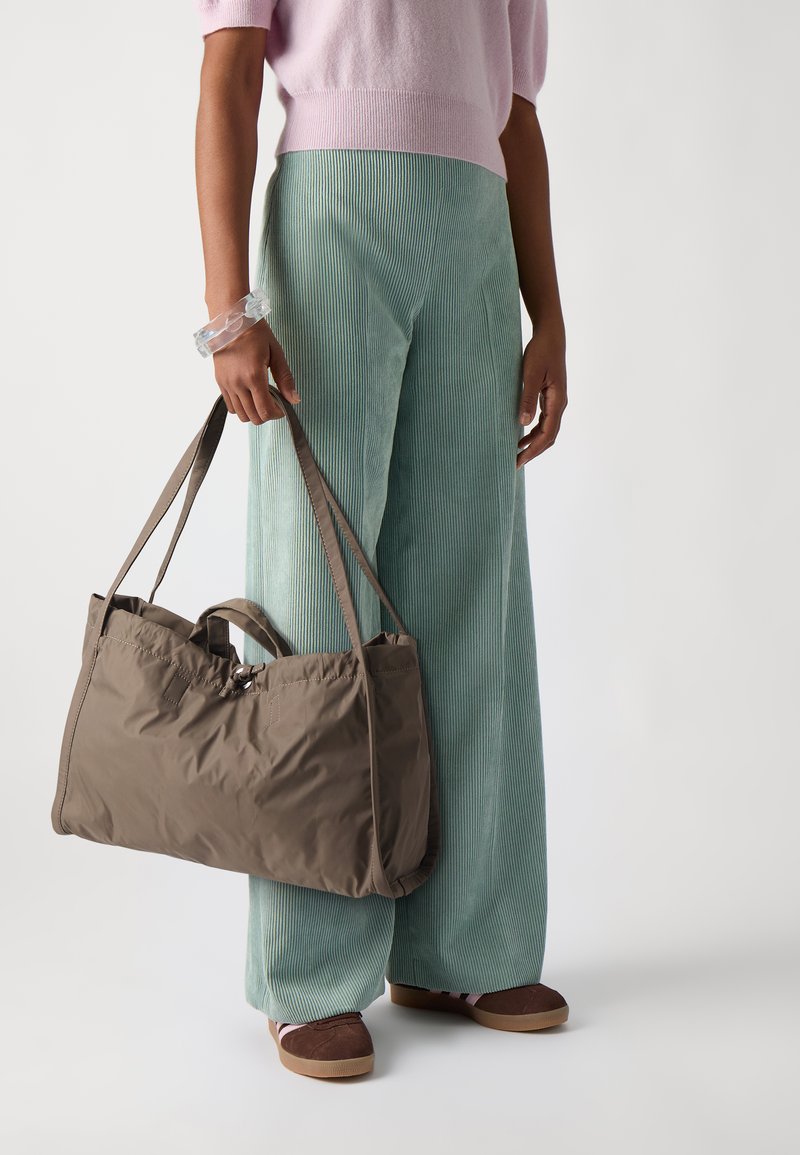 Bruine nylon tote bag met dubbele handvatten, een gladde textuur en een veilige sluiting. Draag met losse mintgroene corduroy broek en bruine schoenen.
