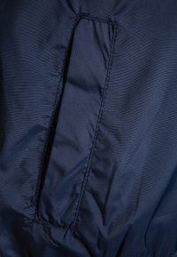 Primer plano de un bolsillo de tela azul marino con abertura vertical y costuras detalladas en una prenda texturizada.