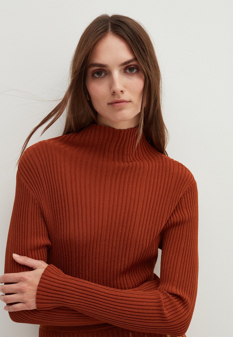 Rostfarbener, gerippter Rollkragenpullover mit langen Ärmeln, der ein strukturiertes Strickmuster und ein hohes Kragen design aufweist.