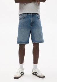 Shorts din denim, de culoare albastru deschis, până la genunchi, cu un design clasic cu cinci buzunare. Asociați cu adidași albi și un tricou gri.
