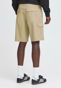 Beige cargo shorts med fire lommer, lige snit og flad talje. Sammen med sorte sko og hvide sokker.
