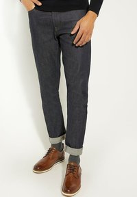 Donkerdenim jeans met een tapered fit, met opgerolde zoom en contrasterende stiksels, gecombineerd met brown leren schoenen en grijze sokken.