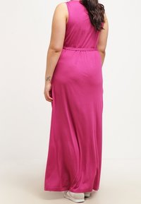 Lang, ærmeløs, tætsiddende maxi-kjole i livlig pink jersey stof. Har en bælte i taljen og falder blidt til gulvet. Minimalistisk design.