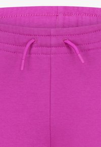 Fuksijas sporta bikses ar savelkamu jostu. Izgatavotas no mīksta auduma ar gludu tekstūru un šūšanas detaļām jostā.