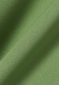 Tissu vert texturé avec un motif de tricotage serré et uniforme, présenté en gros plan avec des plis doux créant des ombres délicates.