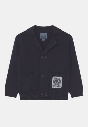 Cardigan en tricot bleu marine avec col, quatre boutons, deux poches avant et un patch logo GUESS rectangulaire sur la poche droite.
