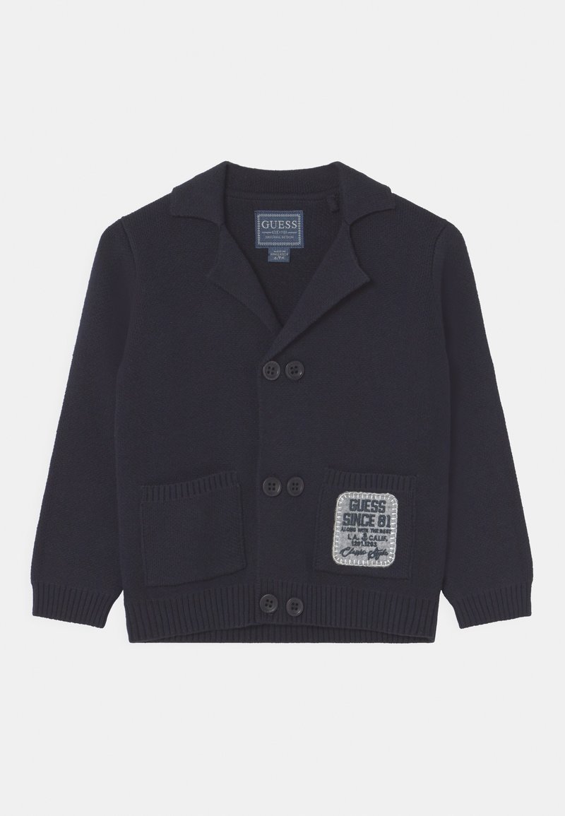 Cardigan en tricot bleu marine avec col, quatre boutons, deux poches avant et un patch logo GUESS rectangulaire sur la poche droite.