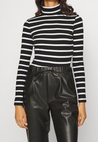 Zwart-witte gestreepte coltrui van ribstof, gecombineerd met hoge zwarte neplederen broek met een trekkoord in de taille.