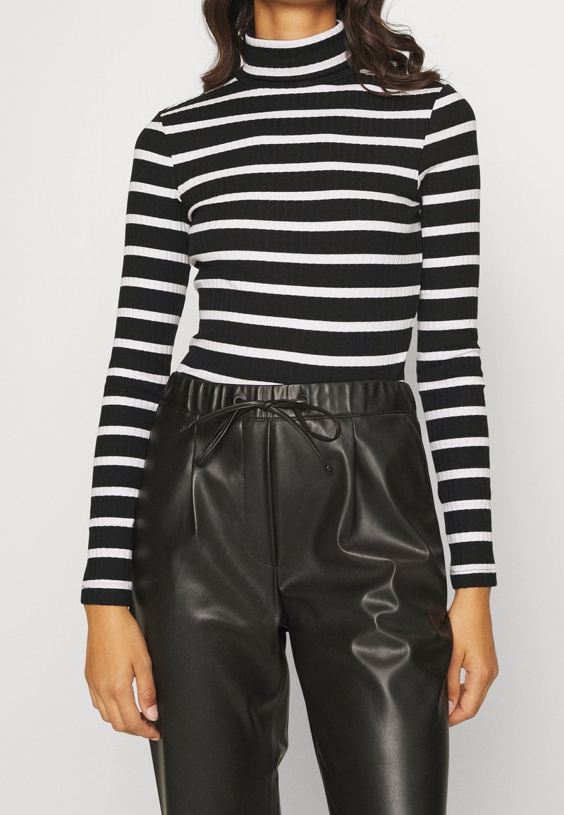Zwart-witte gestreepte coltrui van ribstof, gecombineerd met hoge zwarte neplederen broek met een trekkoord in de taille.