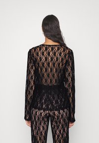 Haut noir en dentelle à manches longues avec un dos transparent, présentant un motif floral complexe et une coupe décontractée, associé à un pantalon en dentelle assorti.