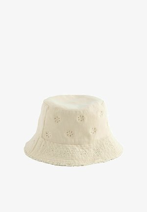 Sombrero tipo bucket de algodón beige con ojales bordados en forma de flores y un borde de ala ligeramente deshilachado, diseñado para un uso casual.