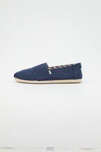 Marineblauwe canvas instapschoen met een afgeronde neus, een beige rubberen zool en een patroon aan de binnenkant. Voorzien van een klein gebrandmerkt label aan de zijkant.