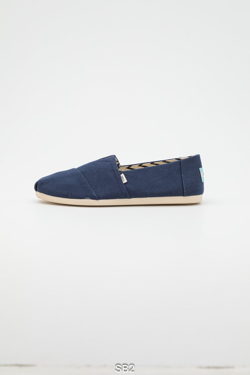 Marineblauwe canvas instapschoen met een afgeronde neus, een beige rubberen zool en een patroon aan de binnenkant. Voorzien van een klein gebrandmerkt label aan de zijkant.