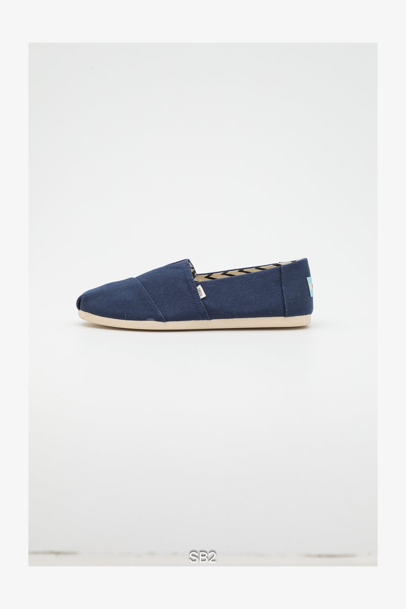 Marineblauwe canvas instapschoen met een afgeronde neus, een beige rubberen zool en een patroon aan de binnenkant. Voorzien van een klein gebrandmerkt label aan de zijkant.