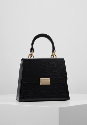 Bolso negro texturizado con forma estructurada, cierre rectangular dorado y asa negra resistente con herrajes dorados sobre una superficie blanca.