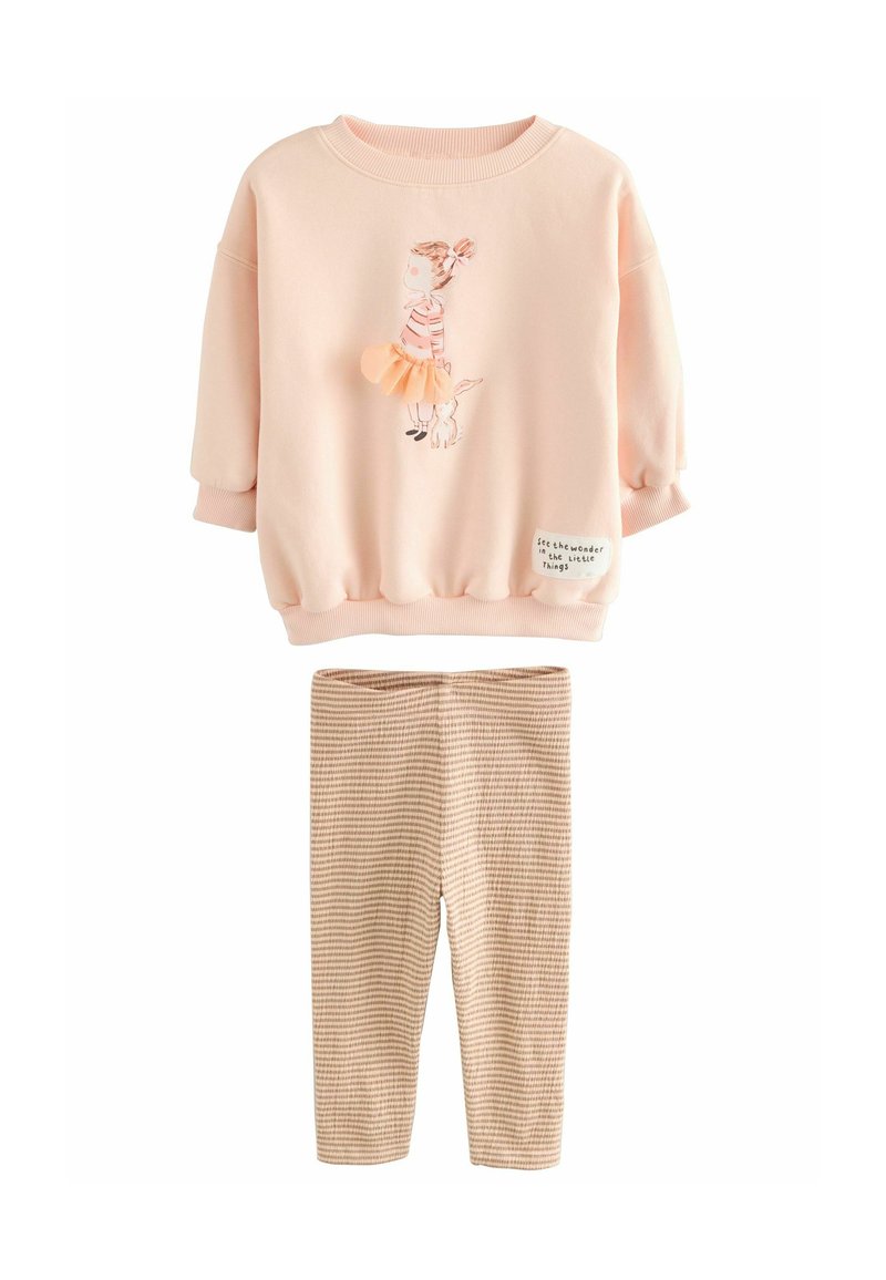 Ljusrosa sweatshirt med grafiskt mönster av en tjej och hund, i kombination med beige rippade leggings. Mjukt, avslappnat material, lätt lös passform.