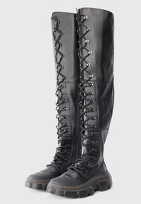 Knee-high black leather boots with lace-up front, chunky rubber sole, and yellow stitching detail. Textured finish and reinforced eyelets.
