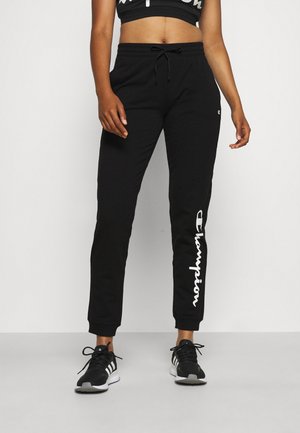 Pantalon de survêtement noir en tissu doux, doté d'une taille élastique avec cordon de serrage et d'un logo "Champion" blanc bien visible sur le côté.