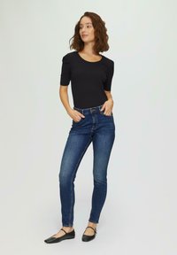 Zwarte gebreide top met korte mouwen gecombineerd met donkerblauwe slim-fit jeans. Het model draagt zwarte flats met een bandje, waarmee een casual outfit wordt getoond.