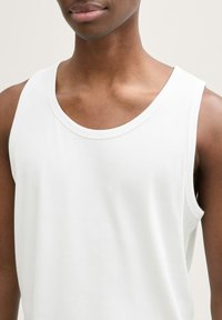 Top alb cu dungi, cu decolteu rotund și fără mâneci, evidențiind o textură netedă și detalii de cusătură uniformă.