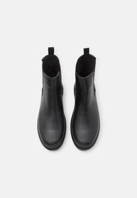 Bottines en cuir noir avec une texture lisse, des bouts ronds et des panneaux élastiques sur les côtés. Comprend des languettes pour un enfilage facile. Semelles plates en caoutchouc.
