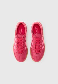 Lyserøde ruskinds sneakers med to lyserøde striber og gummisål. Har en forlænget tå, flade snørebånd og polstret krave for komfort.