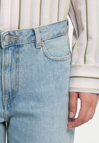 Lys blå denimjeans med en klassisk femlommers design, synlige sømmer og en knappelukking i livet.