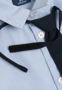 Camicia a righe blu chiaro con bottoni bianchi, dotata di una cravatta in tessuto nero e di una chiusura in Velcro, che offre un design strutturato e a strati.