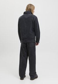 Sort denimjakke med høj krave og matchende løstsiddende sorte bukser. Stoffet har en struktureret finish med subtile sliddetaljer.