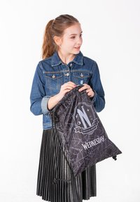 Černý stahovací batoh s motivem pavoučí sítě a textem "STŘEDA". Vyrobeno z lehkého materiálu, obsahuje šňůrkový uzávěr a dekorativní grafiku.