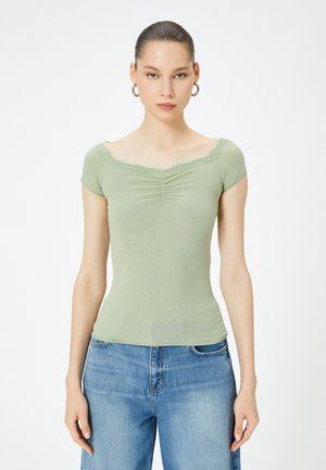Lys grøn ribbet top med kapærmer, V-hals udsmykket med blonder, med frontfolder for struktur. Kombineret med blå denimbukser.
