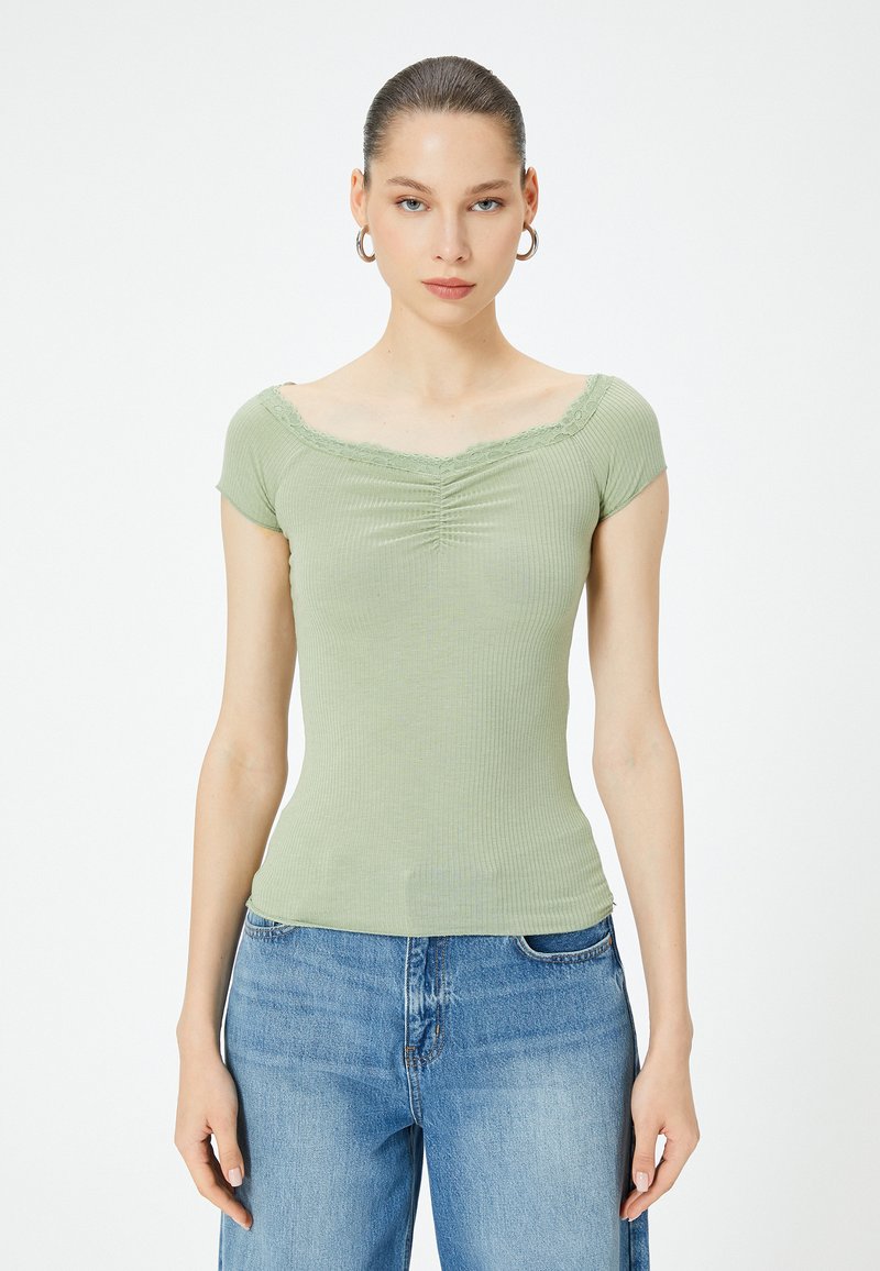 Top a coste verde chiaro con maniche a cappuccio, scollatura a V decorata con pizzo, caratterizzato da pieghe frontali per aggiungere texture. Abbinato a pantaloni di denim blu.