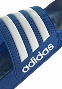 Plave klizne sandale s teksturiranim trakama koje imaju tri bijele pruge. Logo "adidas" u bijeloj boji smješten na plavoj podlozi. Glatka površina.