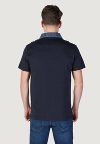 Polo shirt a maniche corte blu navy con colletto azzurro in contrasto che presenta un testo logo; realizzato in tessuto morbido, design minimalista.