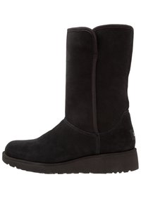 Czarny zamszowy botek do połowy łydki z zaokrąglonym noskiem, miękką fakturą, minimalnymi przeszyciami i płaską gumową podeszwą. Prosty design bez widocznych elementów metalowych.