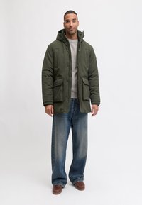 Roheline kapuutsiga polsterdatud jakk, kahe esitaskuga, kombineeritud helesiniste laiade säärtega teksade ja pruunide libisevate kingadega. Märgatavad tekstuuriga kangadetailid.