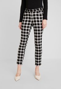 Pantalons à carreaux noir et blanc avec une coupe ajustée, dotés d'une taille mi-haute, de poches latérales et d'une coupe au niveau de la cheville. Texture de tissu lisse.