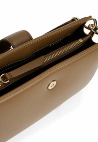 Torebka skórzana w odcieniu brązowym z gładką fakturą, z kieszenią na zamek błyskawiczny i złotymi elementami ozdobnymi. Widok z góry ukazuje przegrody wewnętrzne.