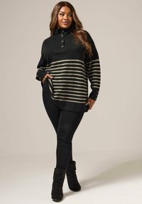 Svart och beige randig tröja med hög krage, knappprodukter och sidofickor, i kombination med svarta slim-fit byxor och ankelskotter.