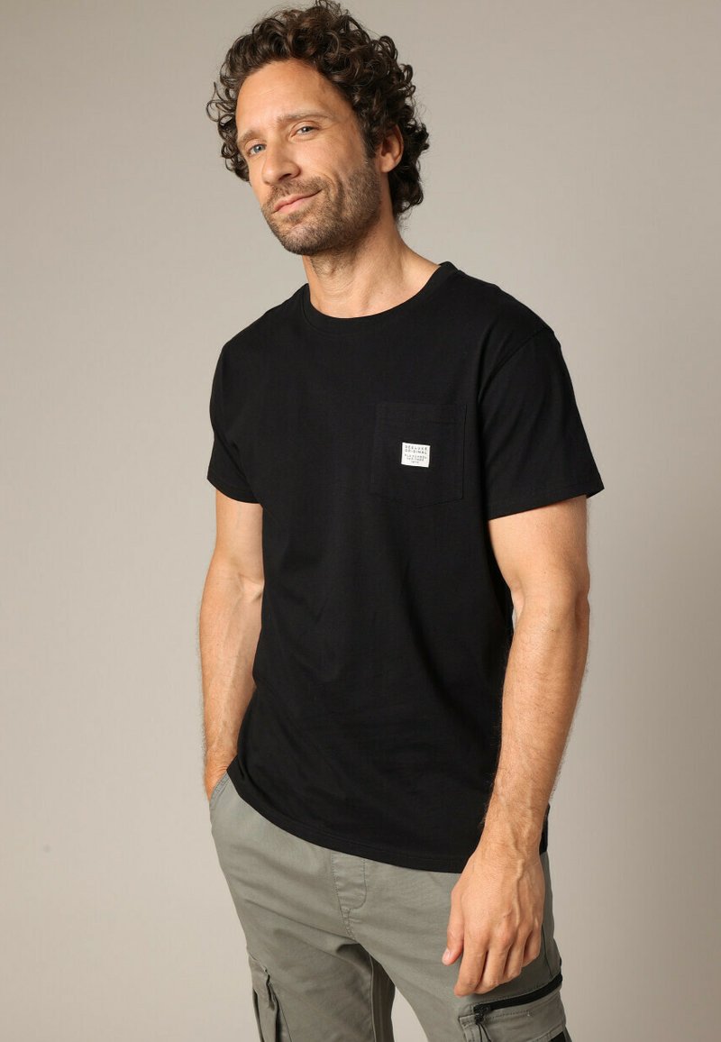 Zwarte t-shirt met korte mouwen, ronde hals en een kleine borstzak met een logo-patch, gemaakt van zachte katoenstof.