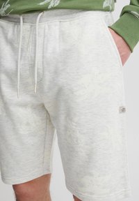 Lysegrå shorts lavet af blødt stof med et diskret mønster af palmeblade. Har elastisk talje med snøre og sidelommer.